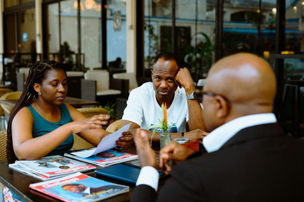 Three people discussing papers at a table in a cafe